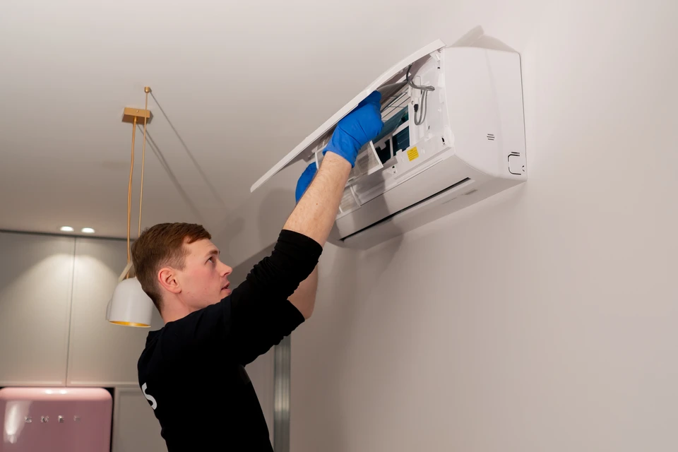 Technicien en combinaison bleue effectuant la maintenance d'une unité intérieure de climatisation split montée au mur