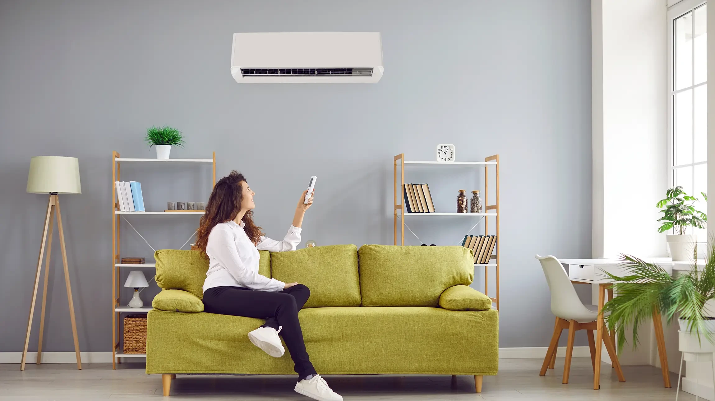 Technicien en casquette bleue et polo blanc effectue la maintenance d'une unité de climatisation murale dans un bureau aux plafonds blancs